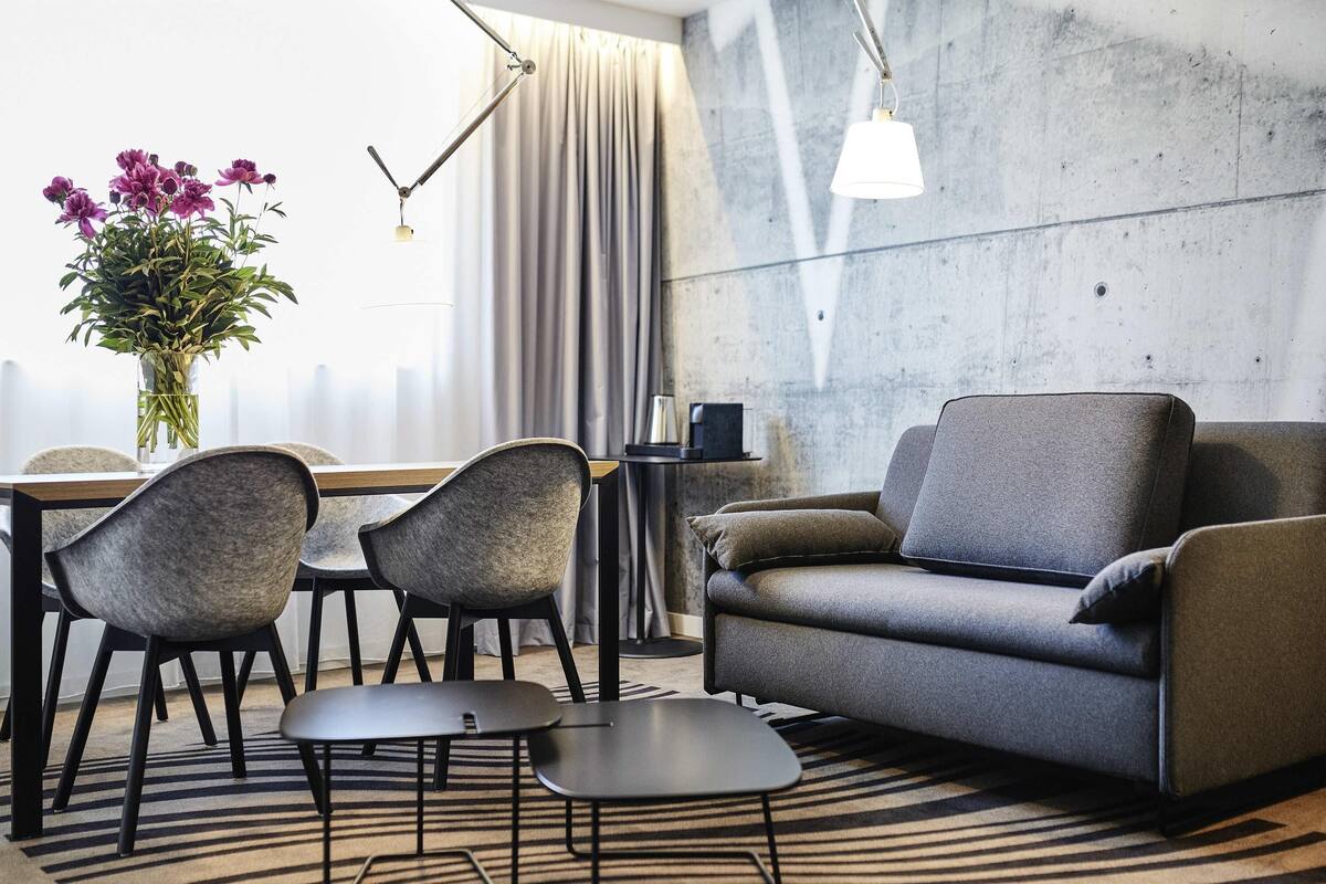 Een moderne woonkamer met een bank, twee stoelen, een kleine tafel, een vaas met bloemen en een lamp.