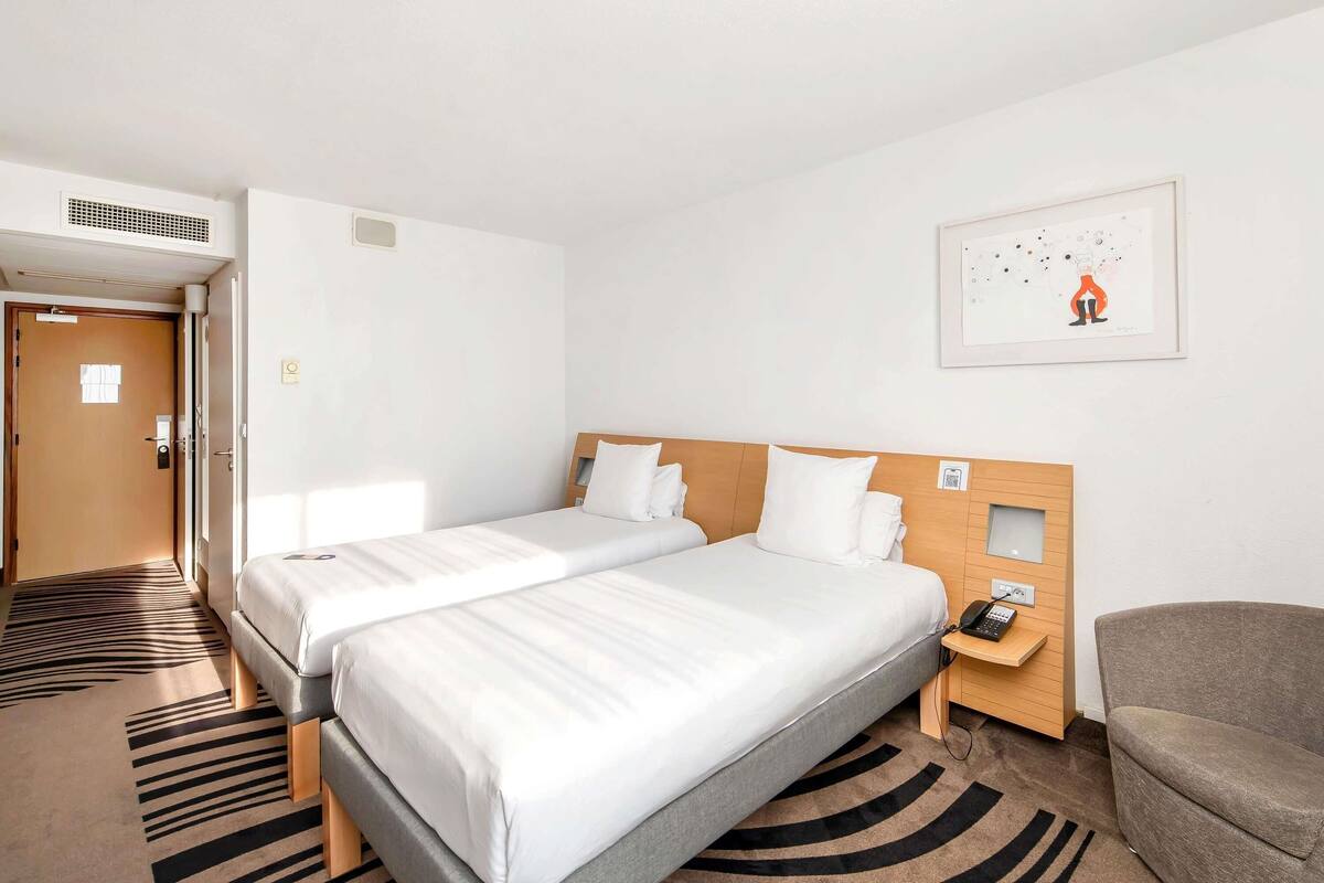 Een hotelkamer met twee bedden, een stoel, een telefoon en een foto aan de muur.
