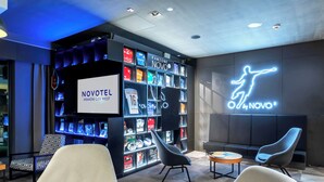 Un hall d’hôtel moderne, avec une enseigne Novotel, une enseigne lumineuse et une exposition de souvenirs sportifs.