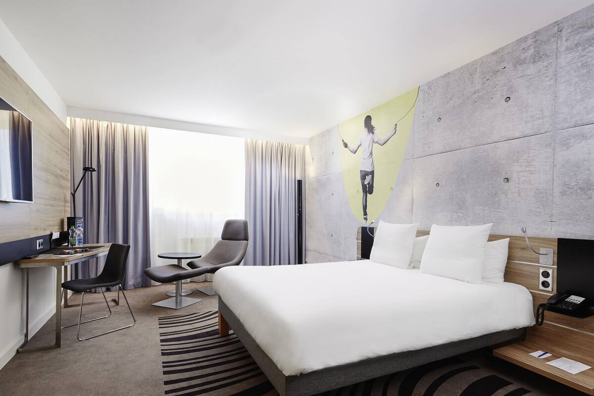 Une chambre d’hôtel moderne avec un grand lit, un bureau avec une chaise, un téléviseur à écran plat et un tableau au mur.