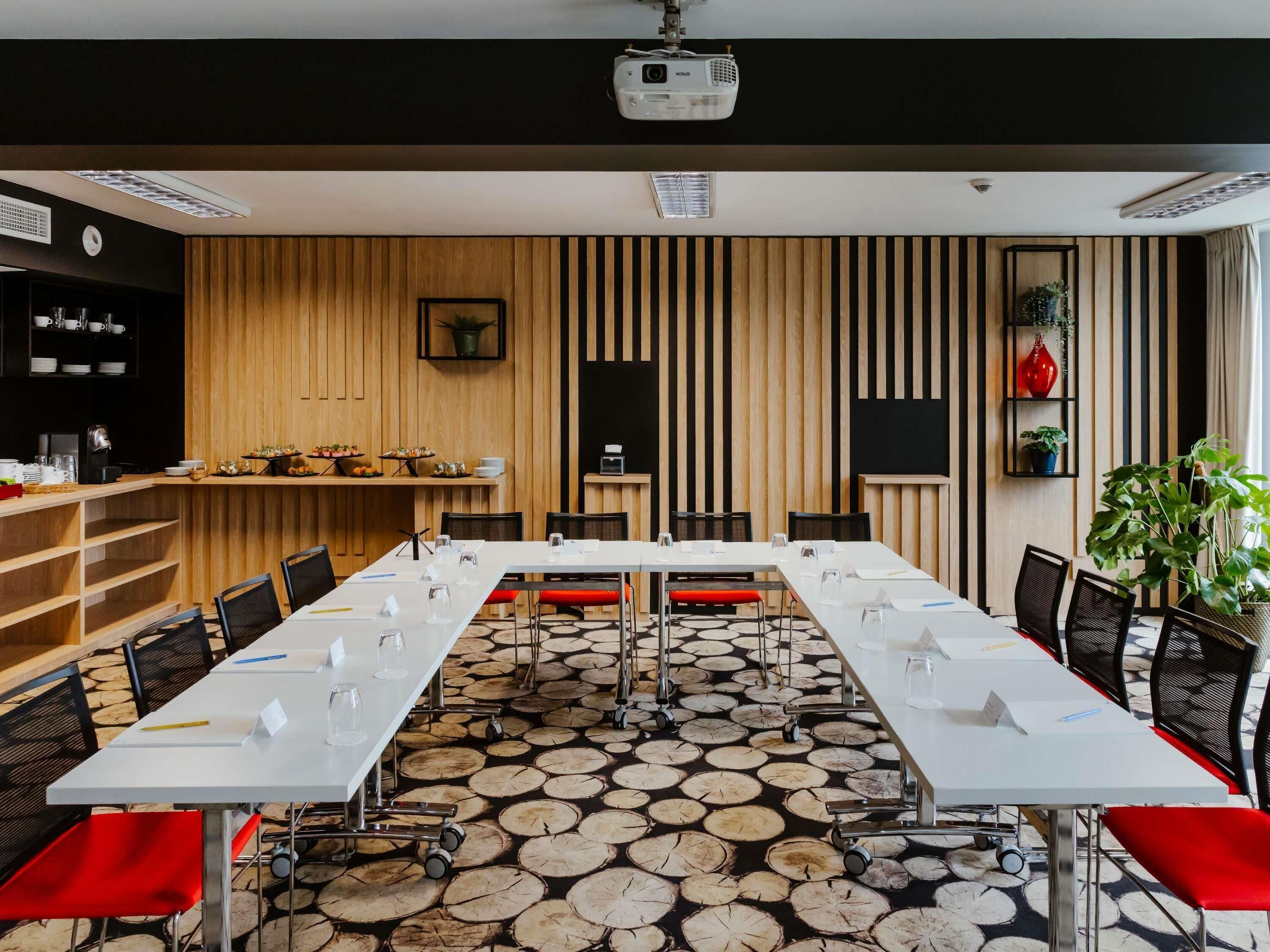 A conference room with a long table, chairs, a projector, and a wooden panel wall.
