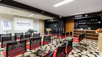 Un salón de conferencias con filas de sillas, una pantalla de proyector y una estación de café.