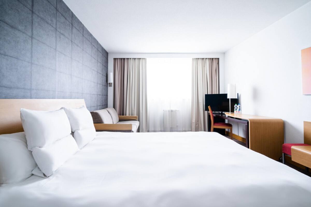 Een hotelkamer met een groot bed, een bureau met stoel, een televisie en een raam met gordijnen.