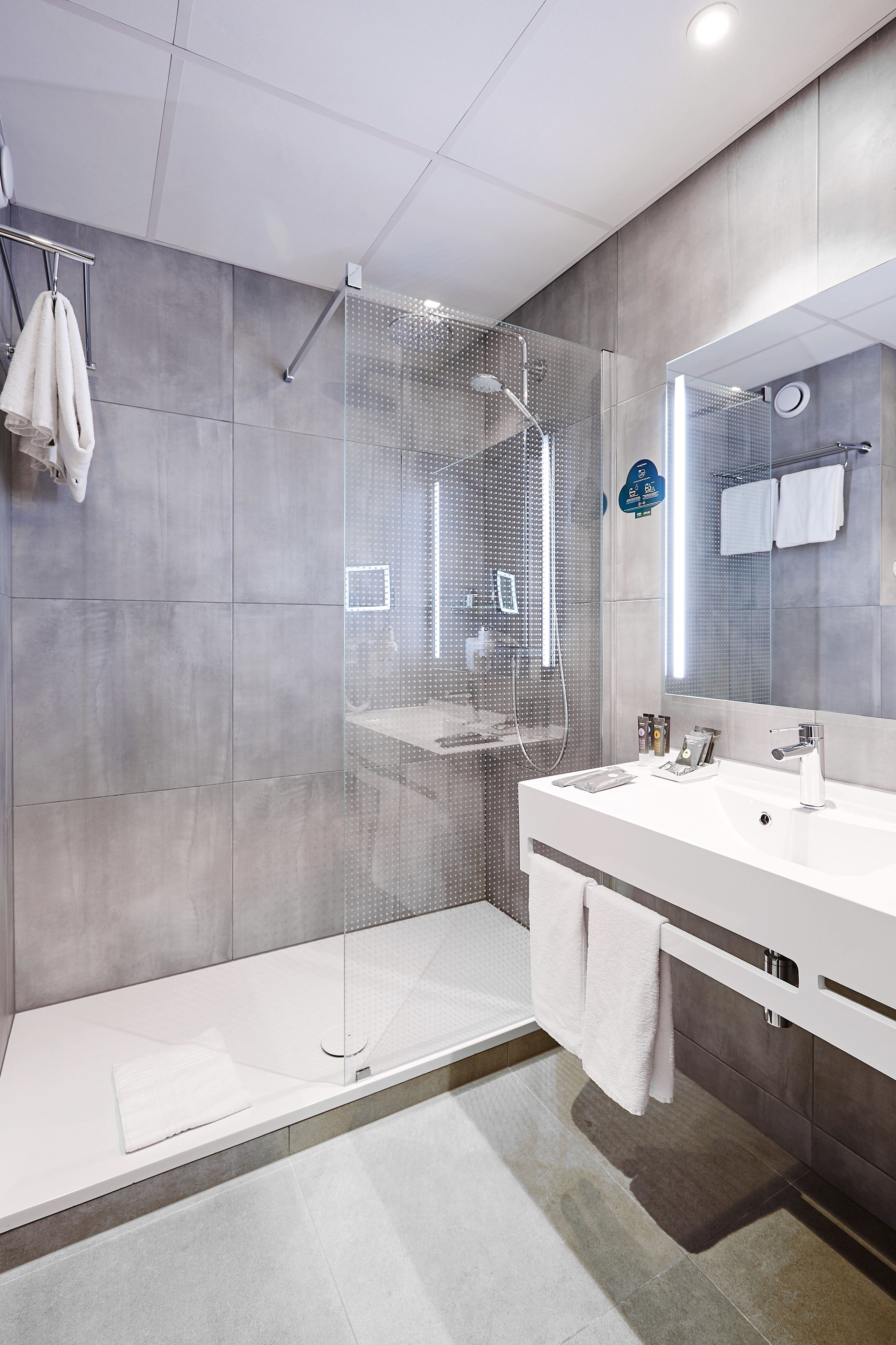 A modern bathroom with a glass-enclosed shower, a white vanity with a large mirror, and a towel rack.