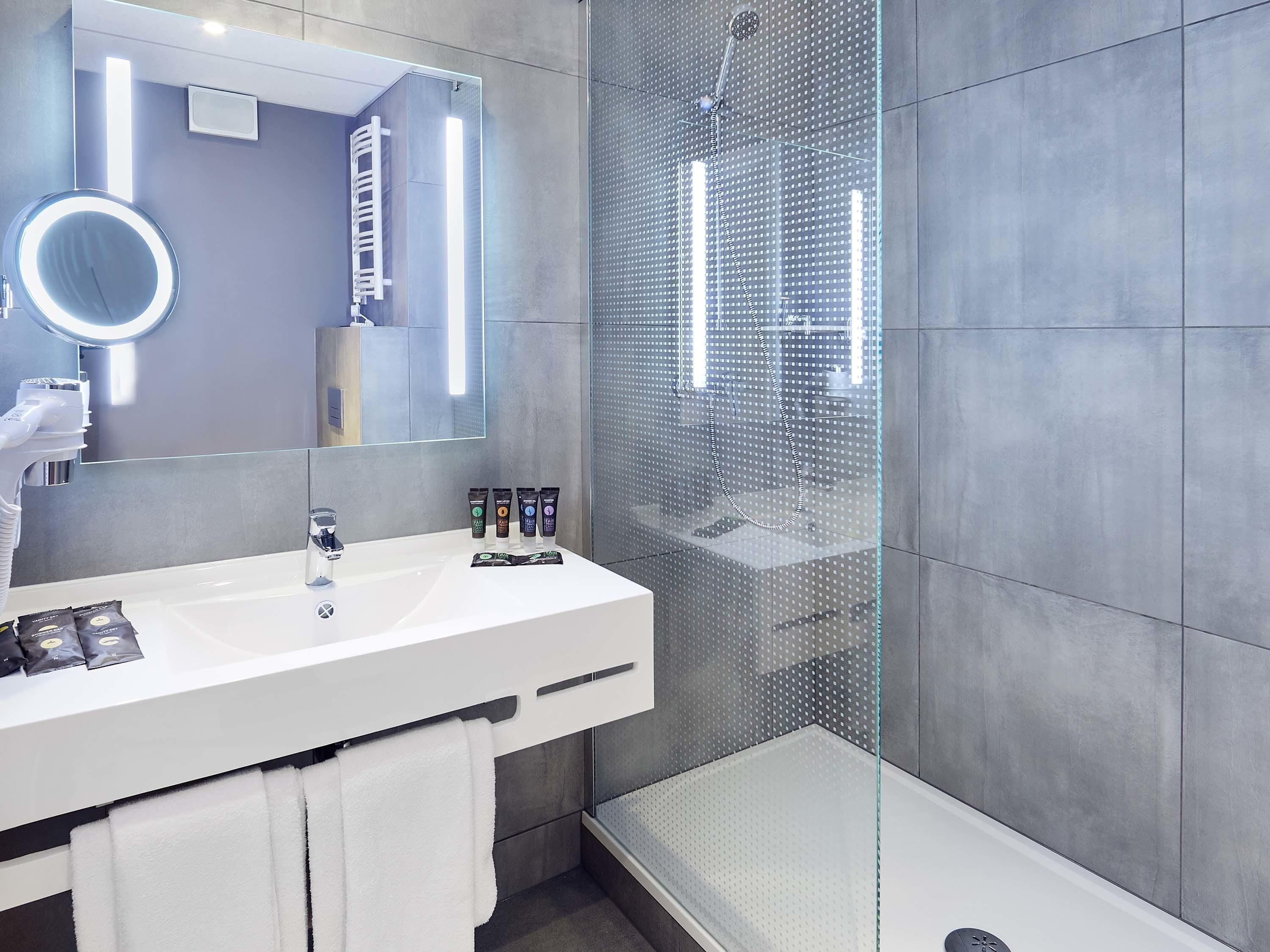 A modern bathroom with a white sink, a large mirror, and a glass-enclosed shower.