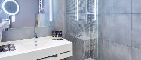 A modern bathroom with a white sink, a large mirror, and a glass-enclosed shower.