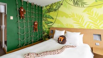 Habitación de hotel con cama, pared verde, pared de escalar con cuerdas y un mural de hojas.