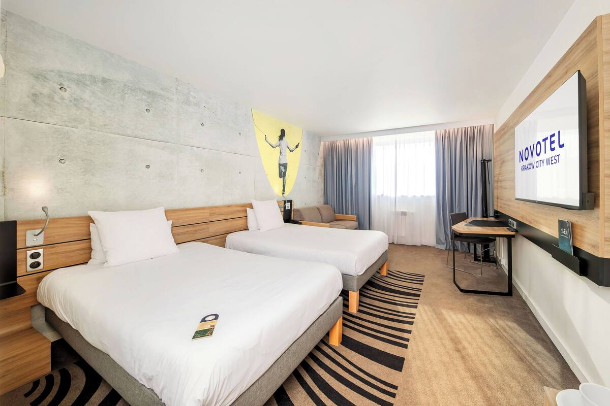 Een hotelkamer met twee bedden, een bureau, een stoel, een televisie en een groot raam met gordijnen.