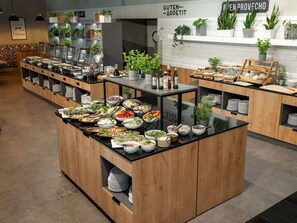 A buffet setup with various food items and drinks, wooden cabinets, and potted plants.