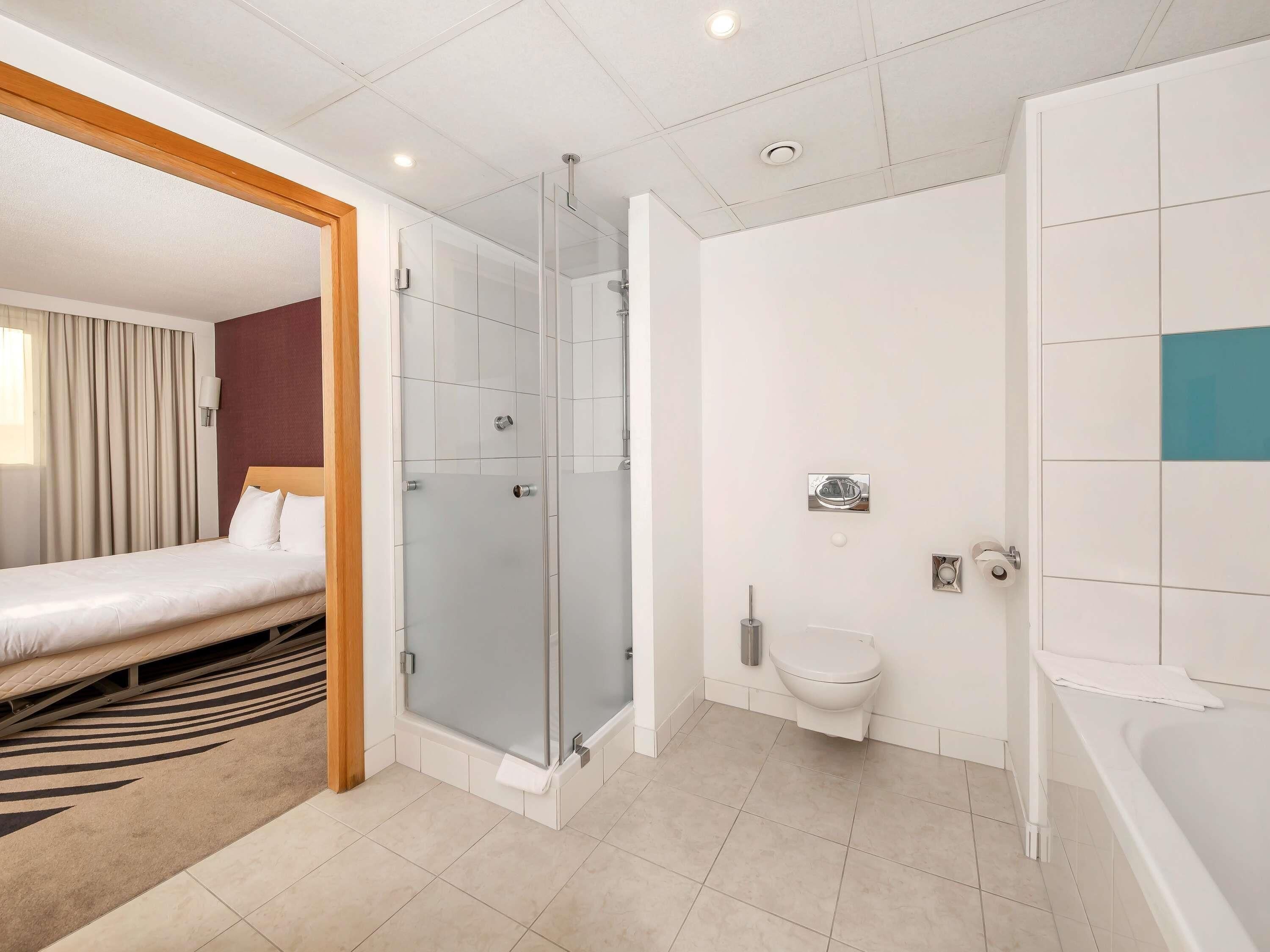 A hotel room with a bed, a shower, a toilet, and a bathtub.