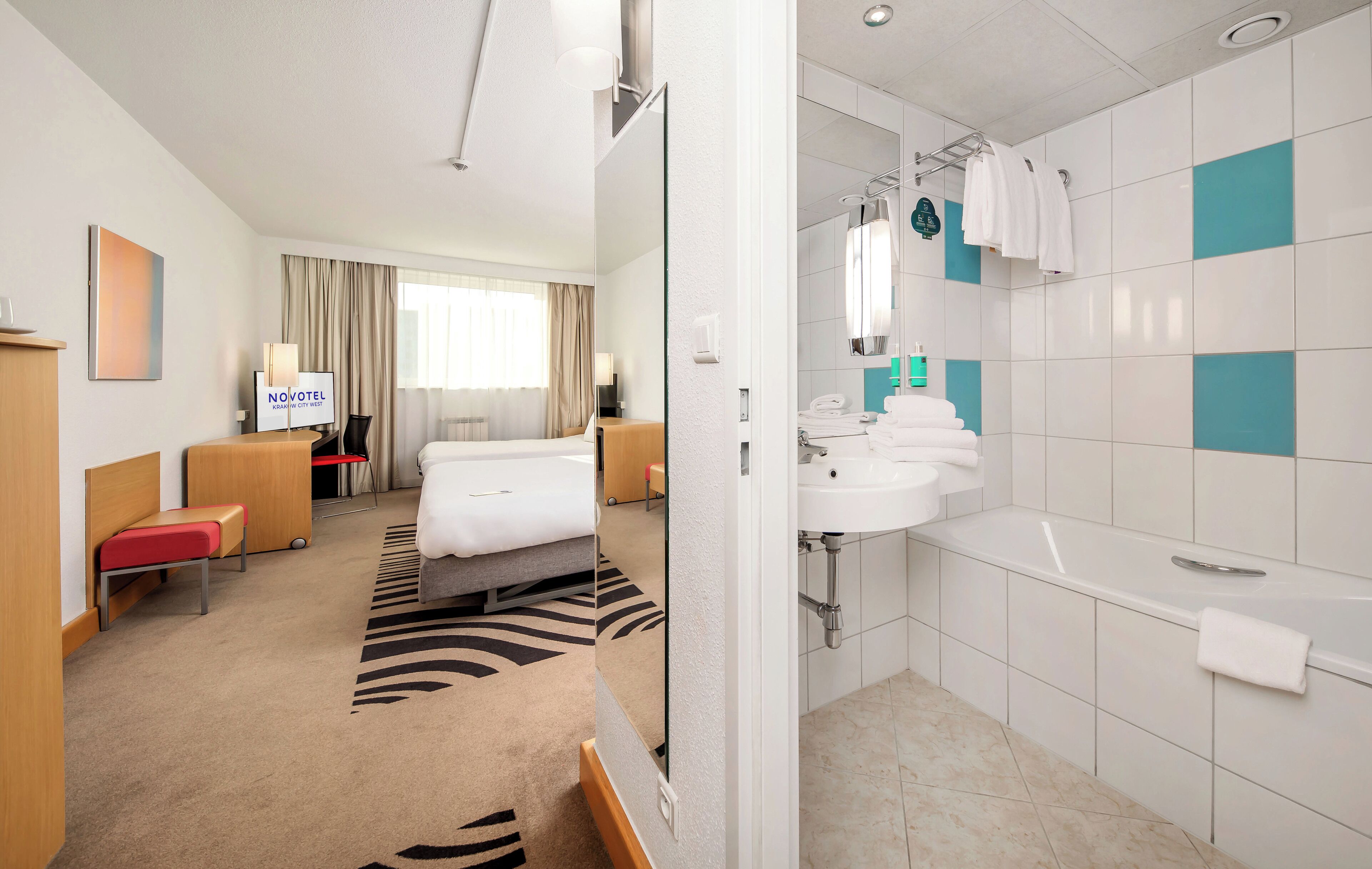 Una habitación de hotel con cama, escritorio, silla, sofá, baño con lavamanos y bañera, y espejo.