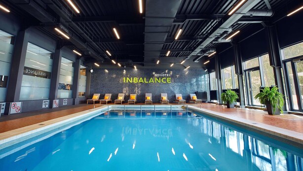 Une piscine intérieure avec des chaises longues, un mur orné du mot « INBALANCE » et de grandes fenêtres.