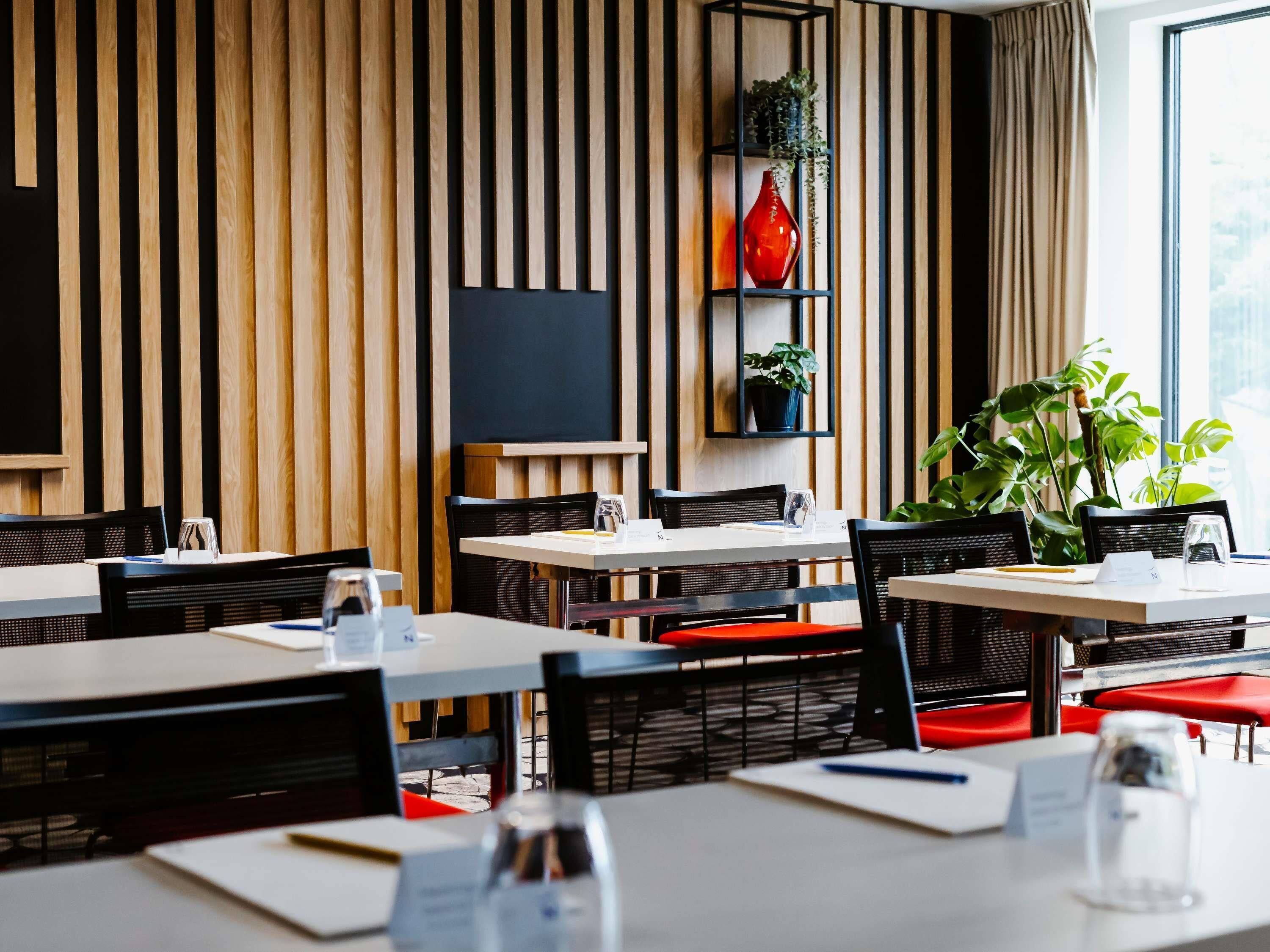 A modern restaurant with wooden panel walls, black shelves, and red chairs.