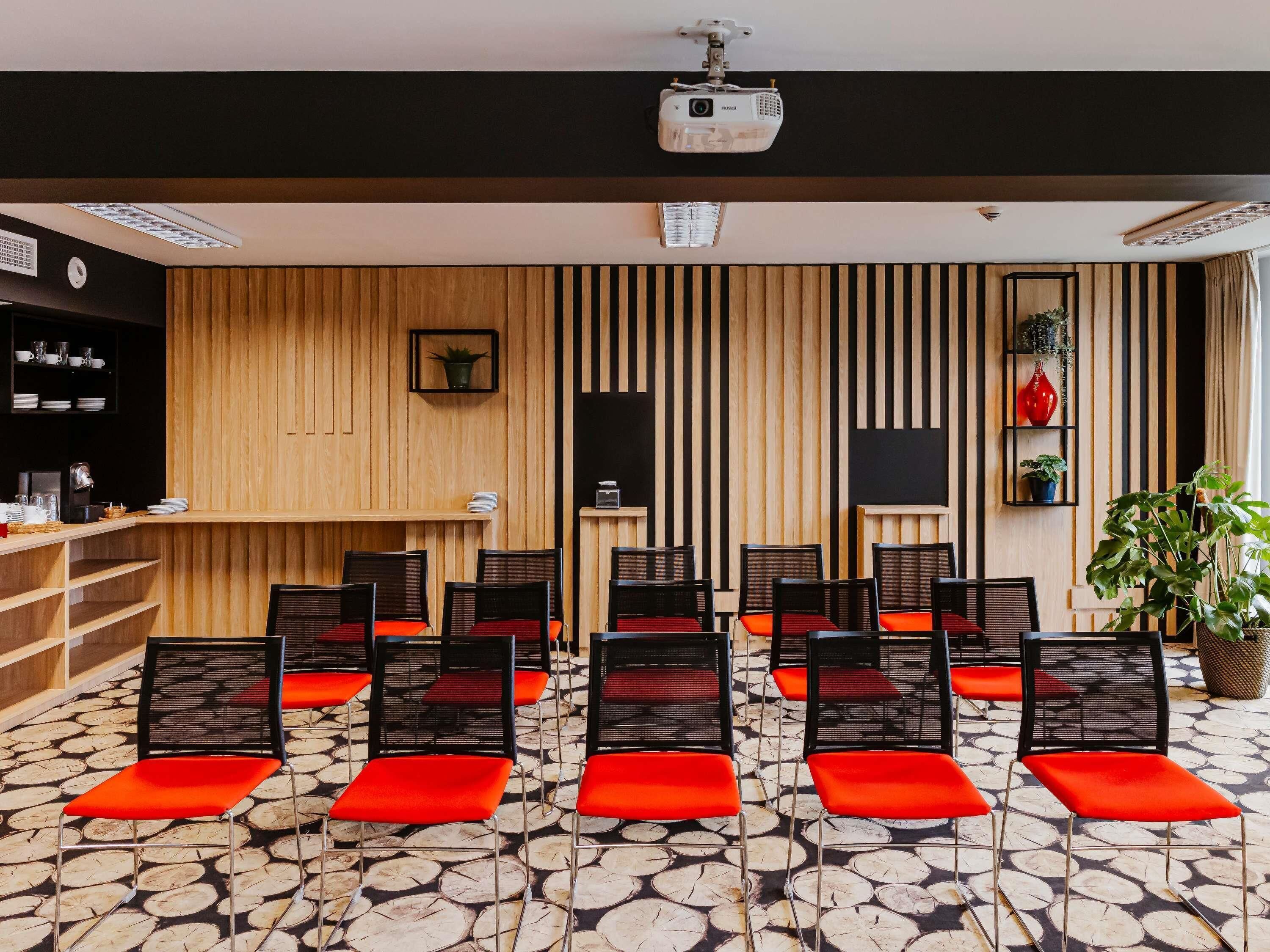 A conference room with a projector, wooden panel walls, and rows of chairs with red cushions.