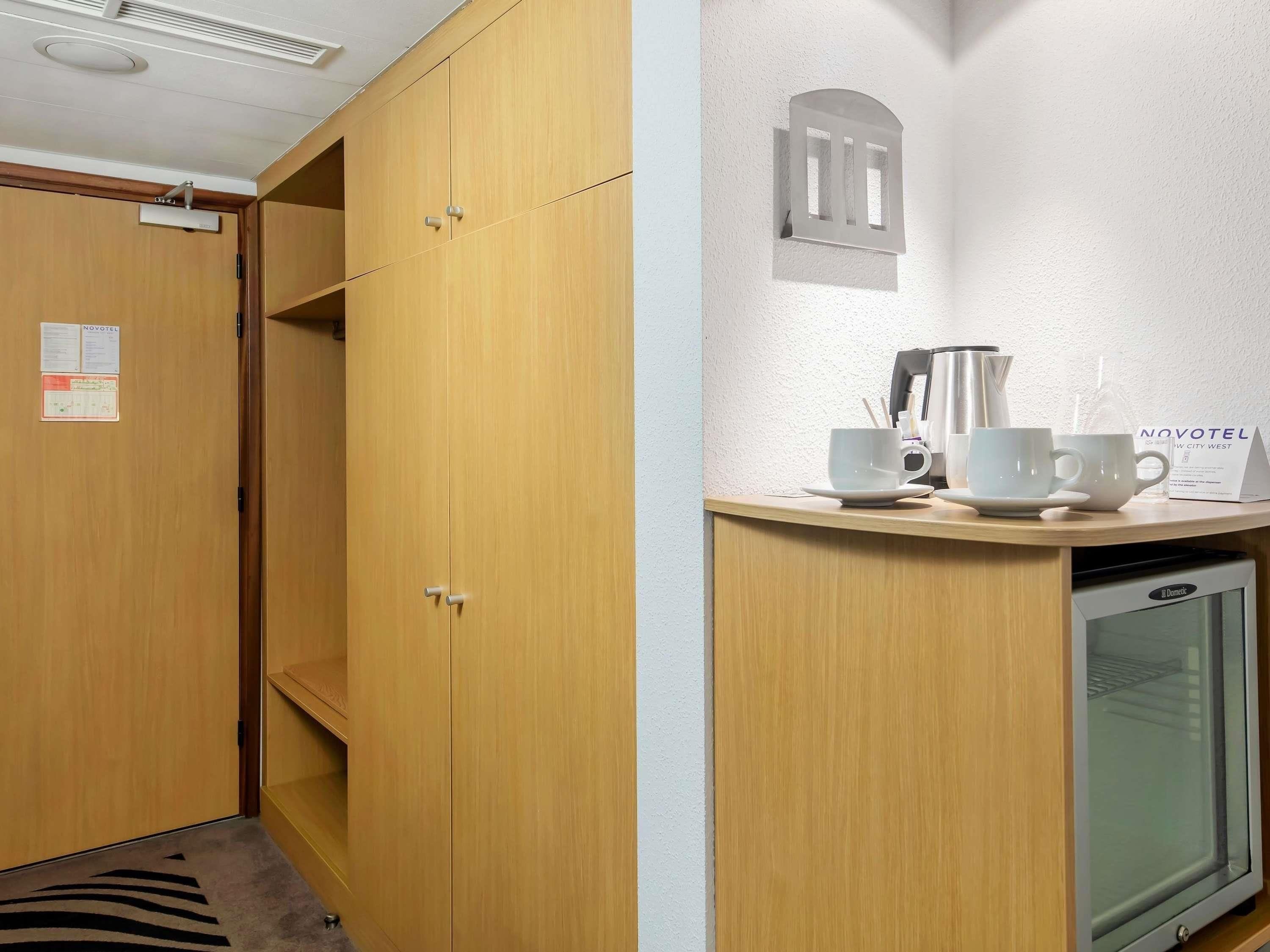 Habitación de hotel con armarios de madera, un minibar y una estación de café empotrada en la pared.