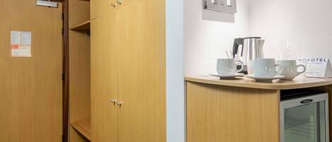 Habitación de hotel con armarios de madera, un minibar y una estación de café empotrada en la pared.