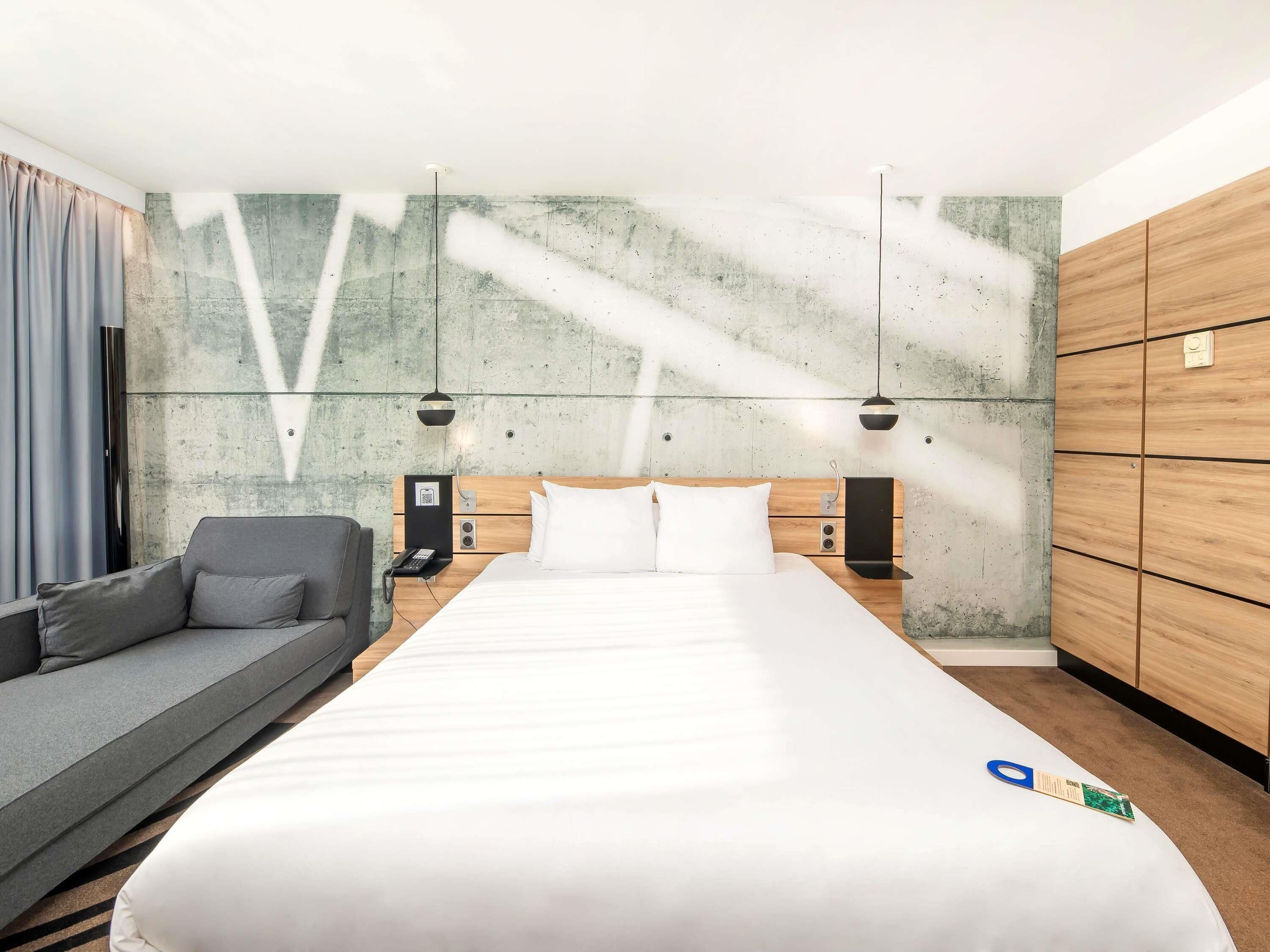 Una habitación de hotel moderna con una cama grande, un sofá, un armario de madera y una pared de concreto decorativa.