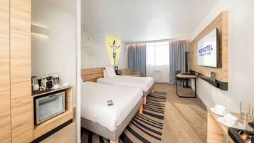 A hotel room with two beds, a desk with a coffee machine, a TV, and a wall-mounted mirror.