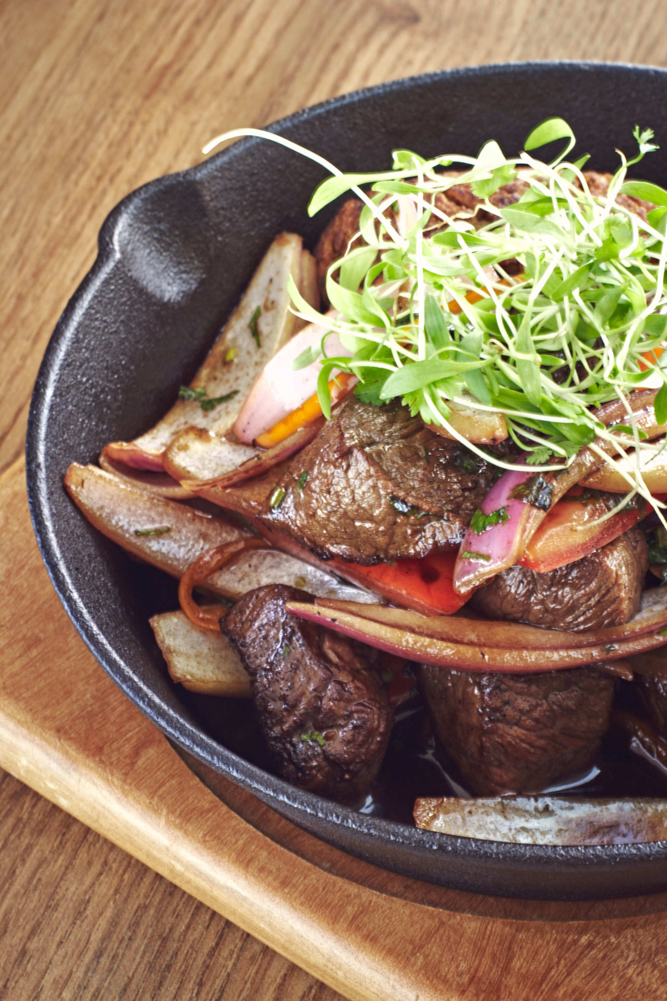 A skillet with steak and vegetables.