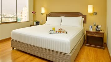 Habitación de hotel con una cama grande, una mesita de noche con lámpara, un teléfono y una bandeja con alimentos para el desayuno.