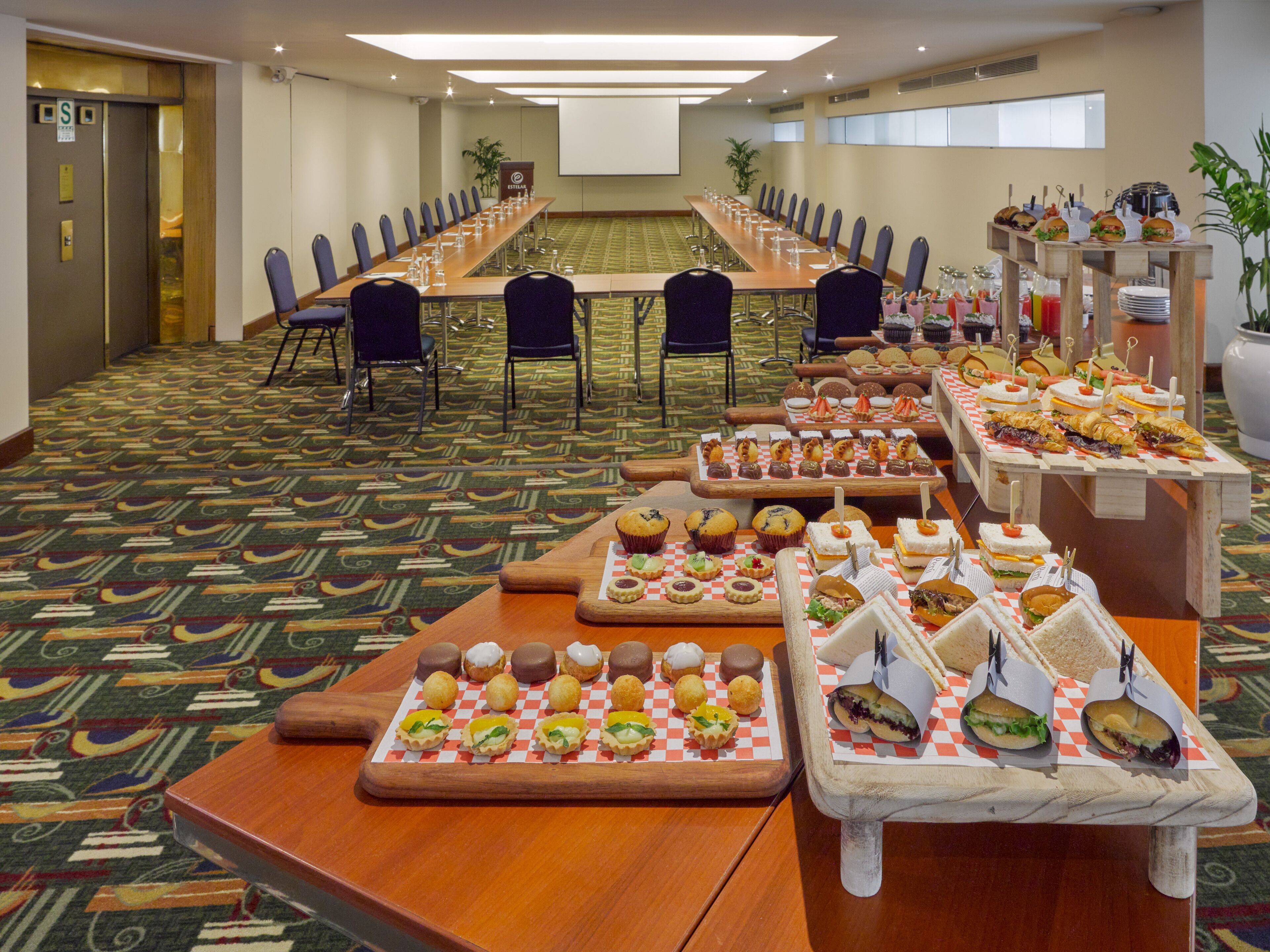 A conference room with a long table, chairs, and a buffet with various snacks and sandwiches.