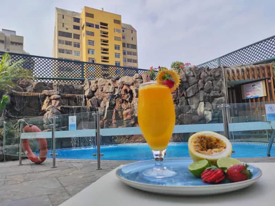 A tropical setting with a pool, a glass of orange juice, and a plate with fruit.