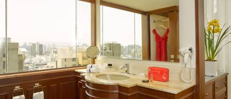 A modern bathroom with a large mirror, a sink, and a hairdryer. There are towels hanging on the wall and a potted plant on the counter.