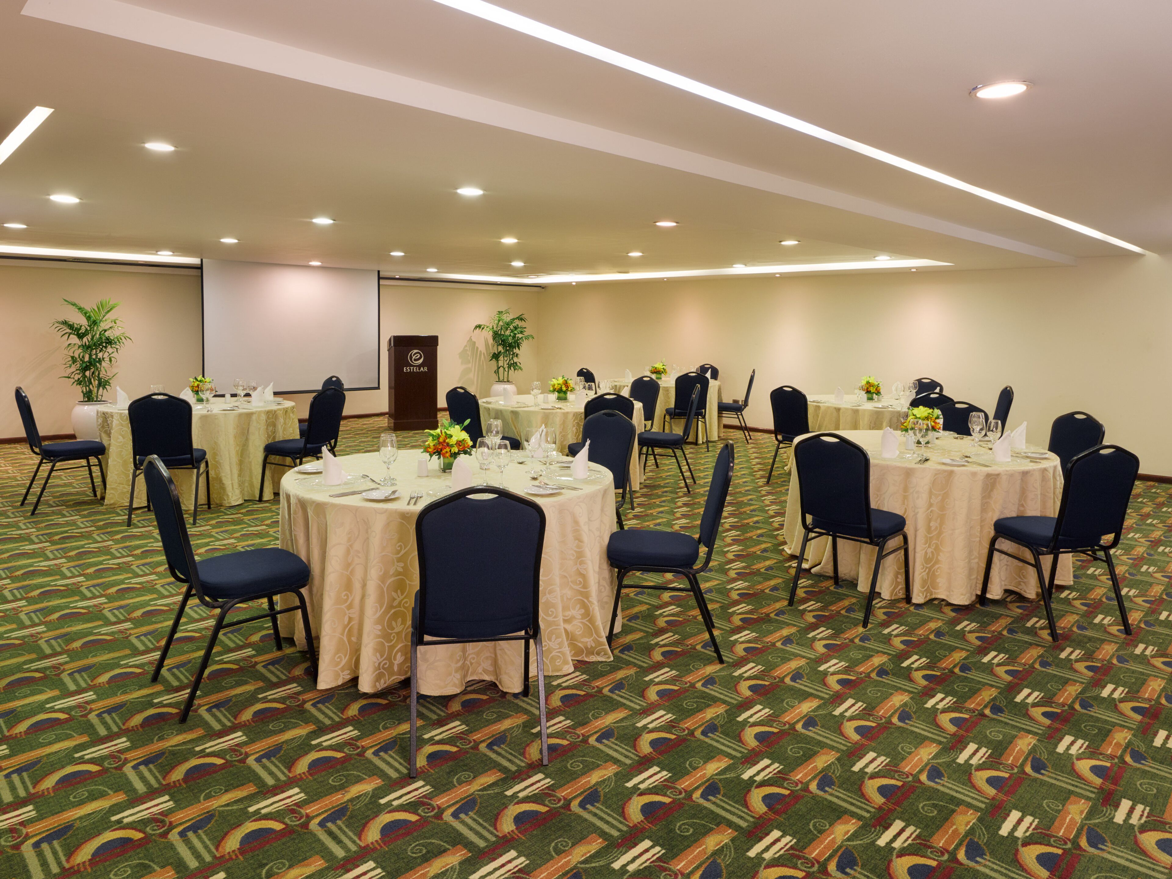 Un salón de conferencias con mesas redondas, sillas y un atril.