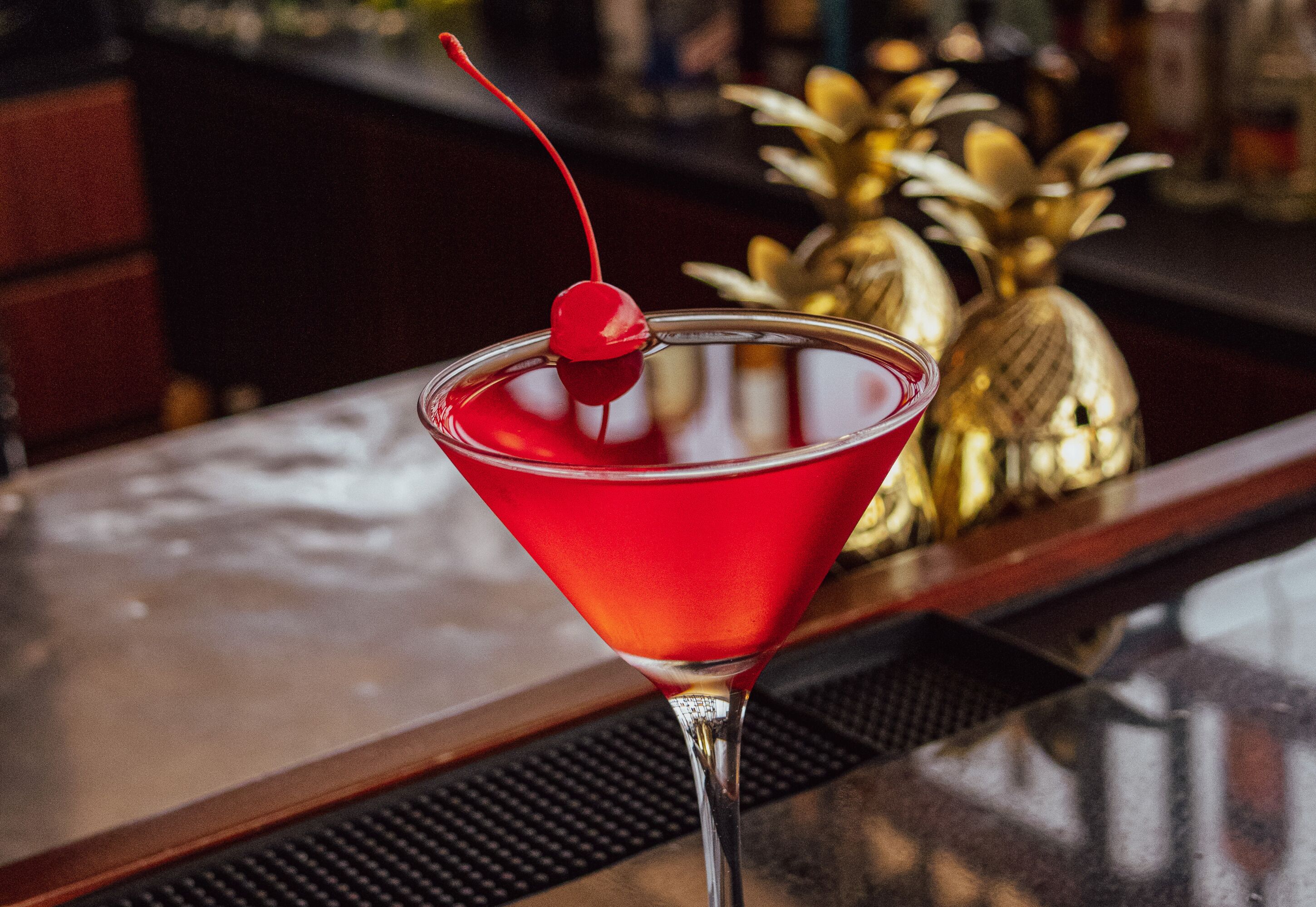 A martini glass with a cherry on a bar counter.
