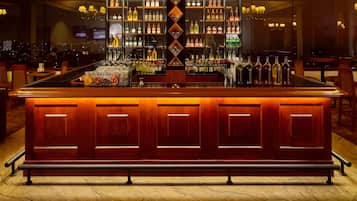 Zona de bar con mostrador de madera pulida, estantes llenos de botellas de licor y vistas a la ciudad a través de amplias ventanas.
