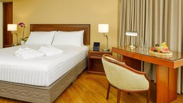 A hotel room with a neatly made bed, a desk with a laptop, a chair, and a fruit bowl on the desk.