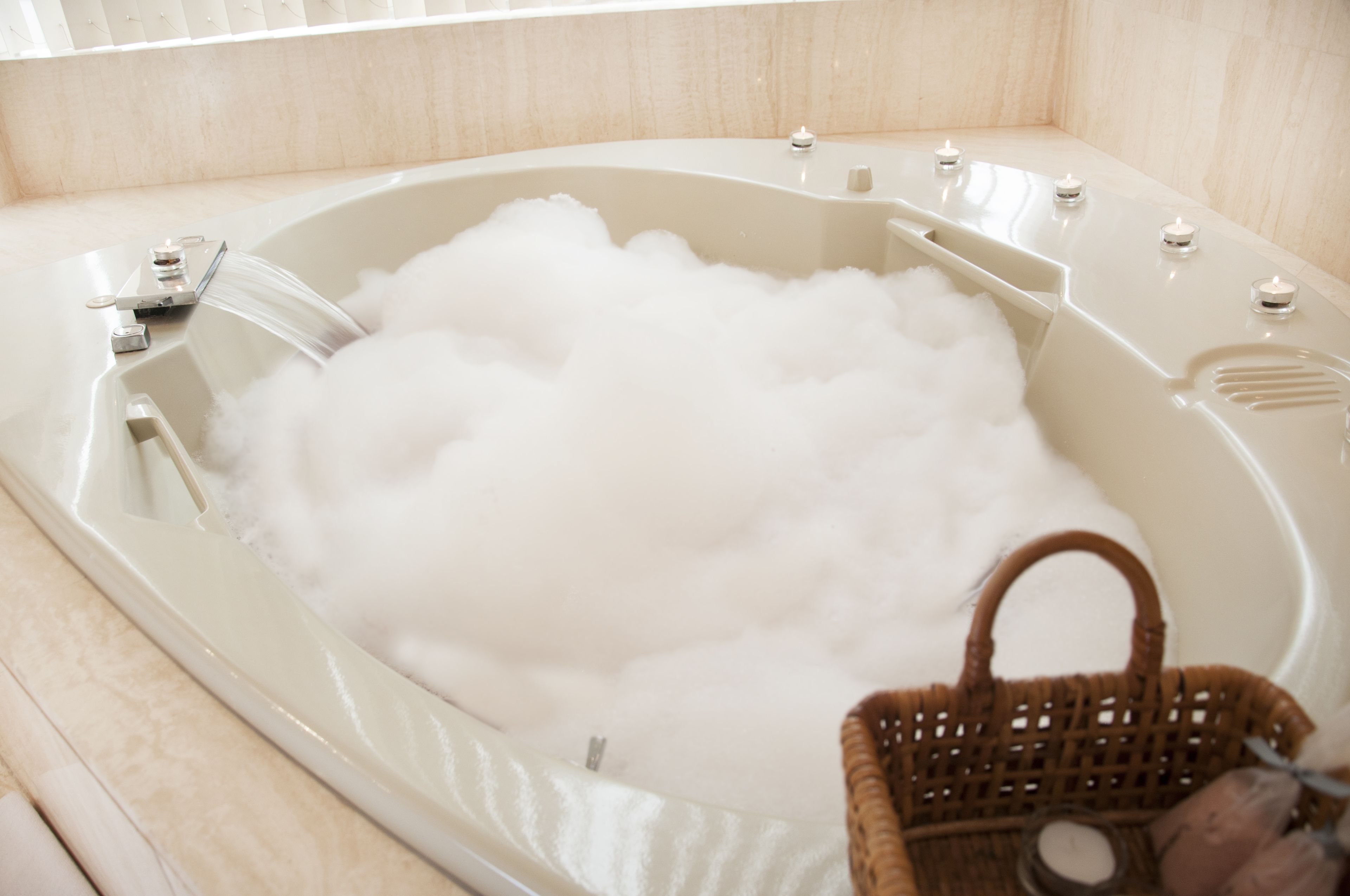 A bathtub filled with bubbles, a faucet, and a wicker basket.