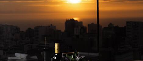 Una mesa dispuesta para dos, con una botella de vino, una servilleta y un plato de vidrio. La palabra “LOVE” está escrita con letras, y hay pétalos de rosa esparcidos sobre la mesa.