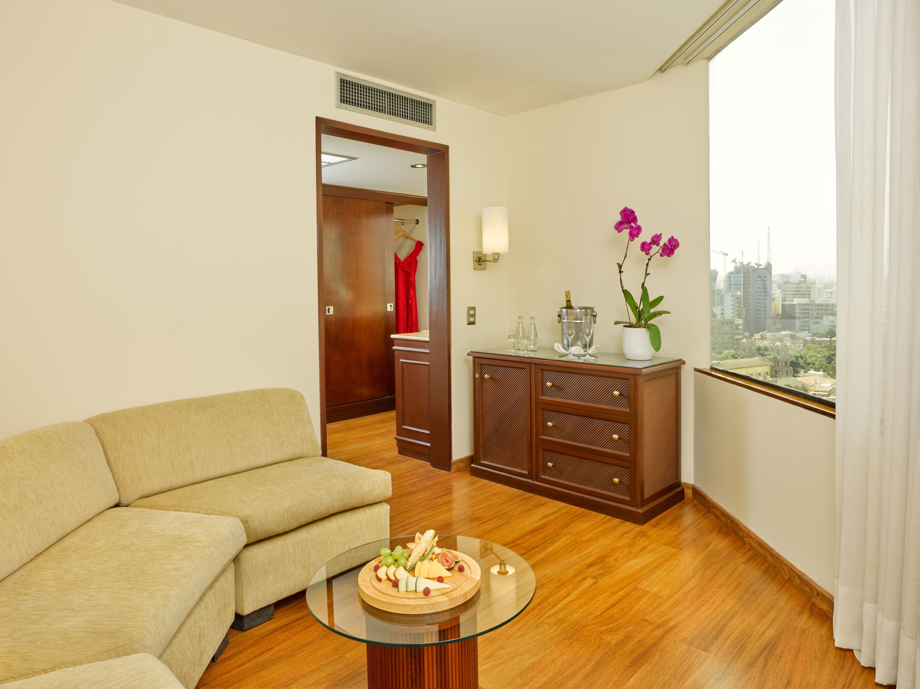Uma sala de estar moderna com um sofá bege, um armário de madeira e uma mesa de vidro com um prato de frutas.