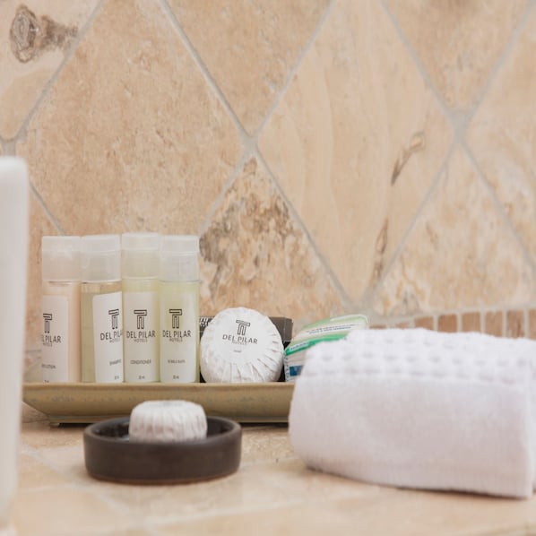 Des articles de toilette sont posés sur le comptoir, notamment des bouteilles de shampoing, d’après-shampoing et de savon, ainsi qu’une serviette et un tapis de bain.