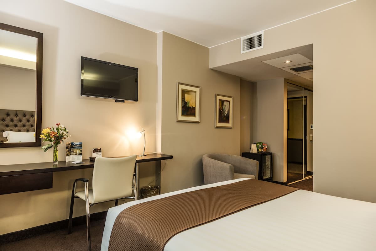 A hotel room with a bed, a desk, a chair, a TV, and framed pictures on the wall.