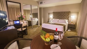 Habitación de hotel con cama, mesita de noche, escritorio con computadora y mesa de comedor con fruta y una copa de vino.