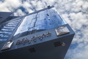 La façade extérieure de l’hôtel Del Pilar, avec son aspect moderne et son parement de verre qui reflète le ciel et les nuages.