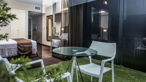 Una habitación de hotel moderna con un separador de vidrio, una mesa redonda de vidrio y una silla de mimbre blanco.