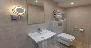 A modern bathroom with a white sink, toilet, and a large mirror with a built-in light.