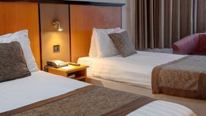 A hotel room with two beds, a bedside table with a phone, and a wall-mounted light. - Best Western Corona (London)