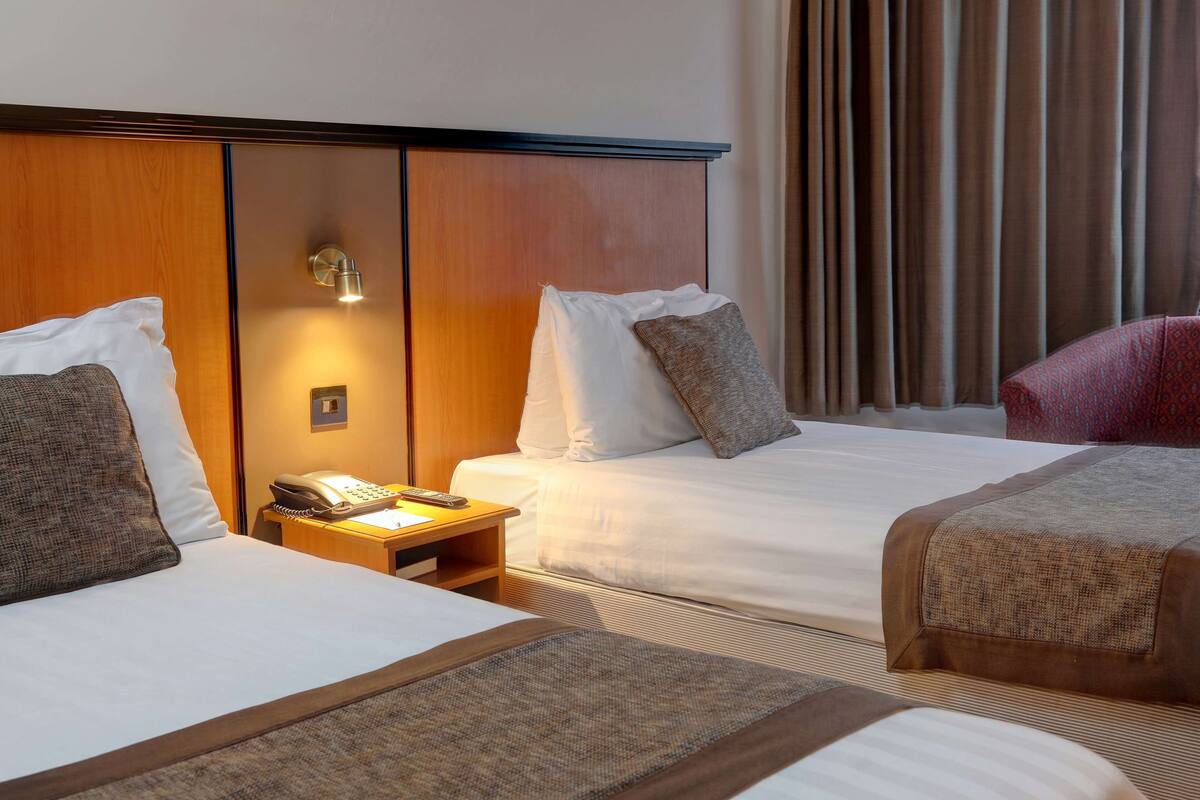A hotel room with two beds, a bedside table with a phone, and a wall-mounted light.