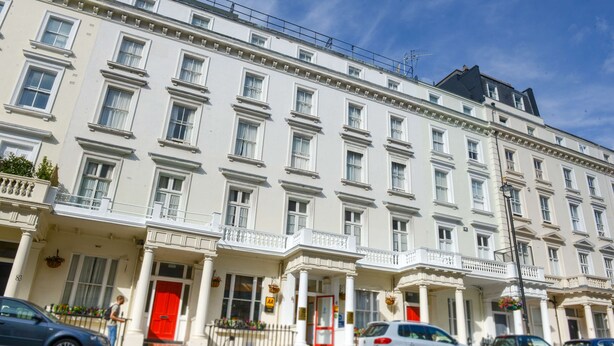 A row of white buildings with multiple windows and a red door. - Best Western Corona (London)