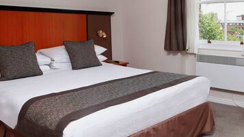 A neatly made bed with a brown bed skirt, a wooden headboard, and a nightstand with a remote control.