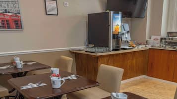 A dining area with tables set for two, a coffee machine, and a counter with food items.