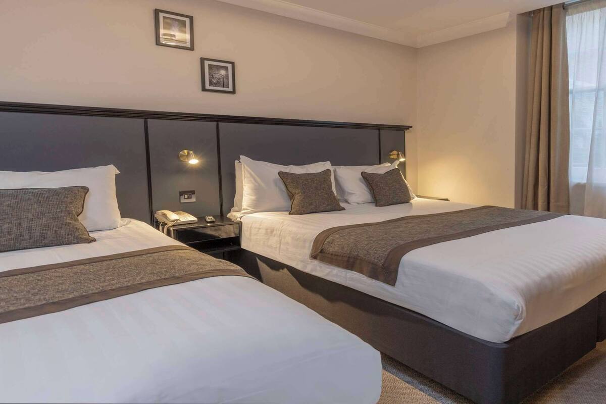 A hotel room with two beds, a nightstand with a phone, and a window with curtains.