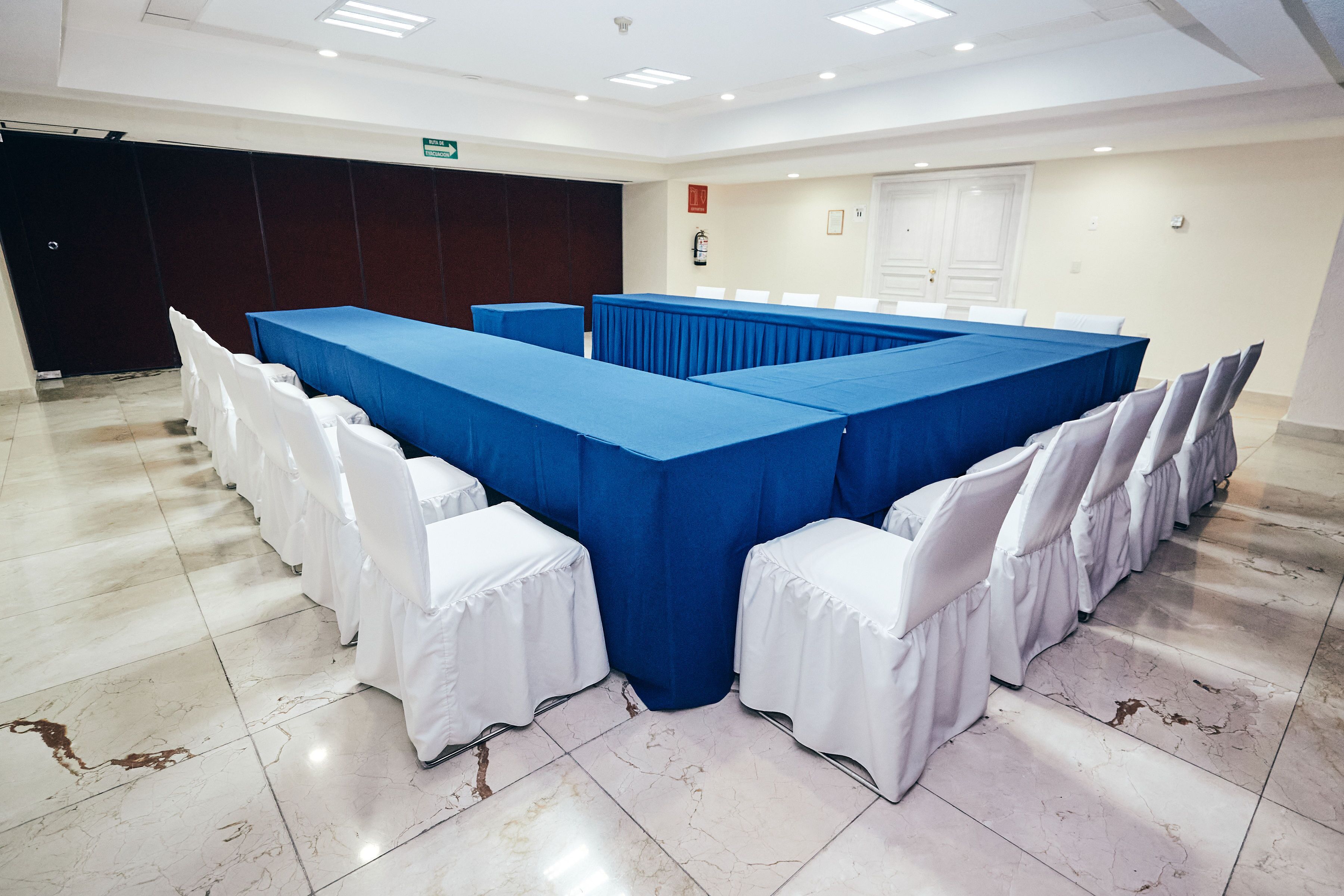 Une salle de conférence avec une grande table bleue, des chaises blanches et un sol en marbre.