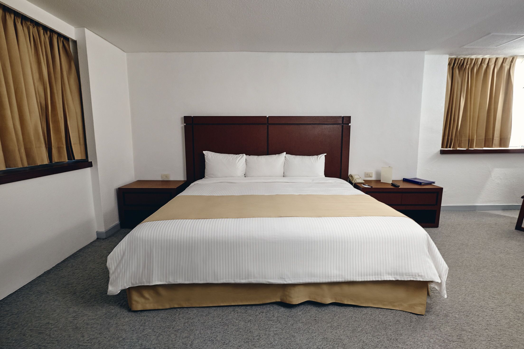Una habitación de hotel con una cama grande, dos mesitas de noche y una ventana con cortinas.