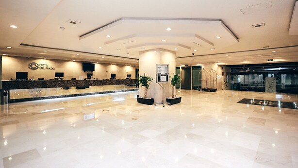A hotel reception area with a marble floor, a reception desk, and a pillar with two potted plants. - Hotel Del Prado (Mexico City)