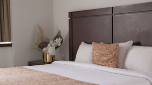 A neatly made bed with a patterned bedspread and pillows, a dark headboard, and a small bedside table with a vase of dried flowers. - Hotel Del Prado (Mexico City)